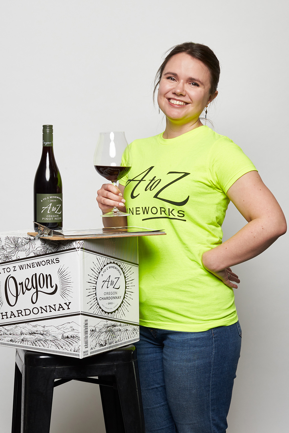 Allison with wine, clipboard and wine bottle on a box sitting on a stool WAAZ