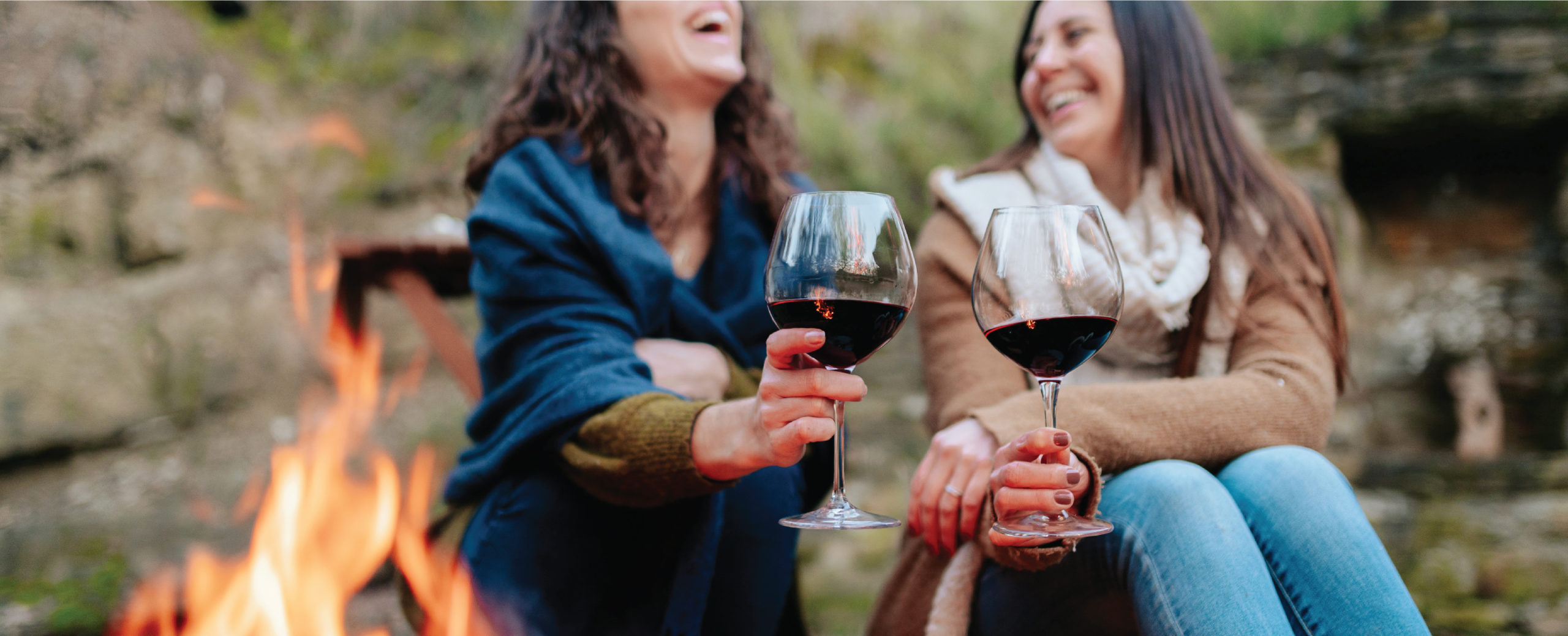 Women by campfire holding wine and laughing