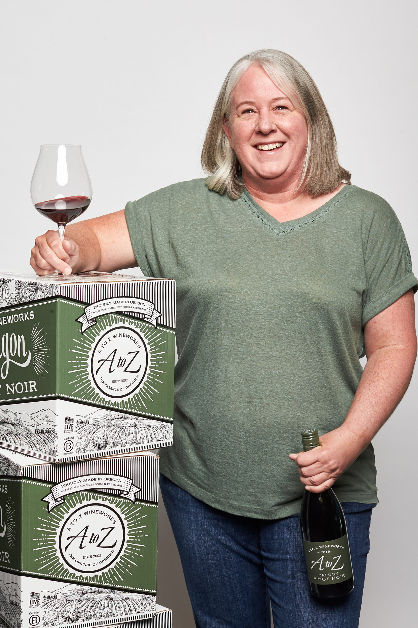 Melisa holding wine glass and wine leaning against Pinot Noir boxes WAAZ